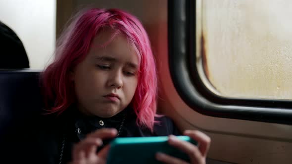 Pretty Modern Little Girl with Pink Hair is Riding Train and Watching Cartoons By Smartphone
