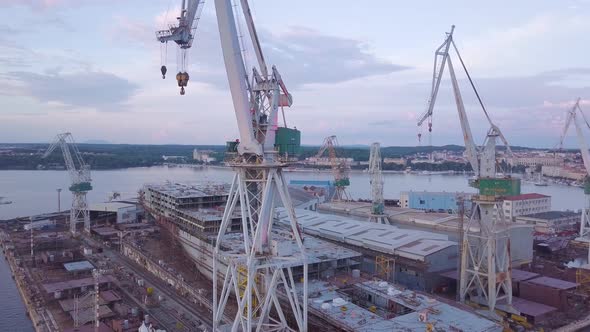 Construction Cranes At The Shipyard With Unfinished Cargo Ship