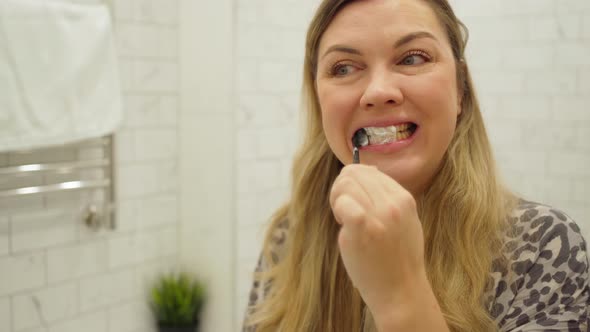 Woman with Long Blond Hair Brushing Her Teeth with Toothpaste in Front of a Mirror