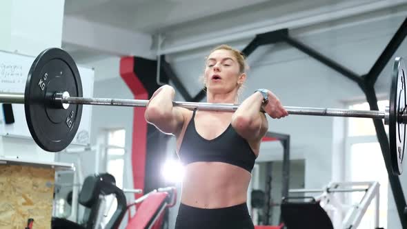 Athletic woman performs traction pose, performing exercises with a barbell