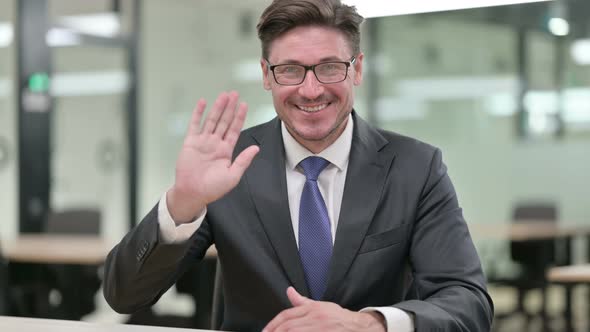 Cheerful Middle Aged Businessman Waving at the Camera 