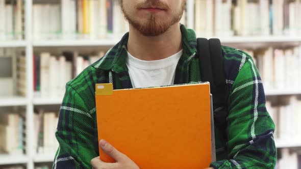 A Young Student with Textbooks in His Hands Is Standing in the Library