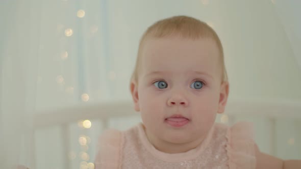 Close Up of 10 Months Old Baby Girl with Blue Eyes Sitting in Bed with Canopy with Lights