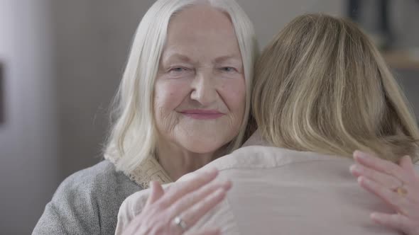 Portrait of Happy Old Caucasian Mother Hugging Daughter at Home Indoors Looking at Camera