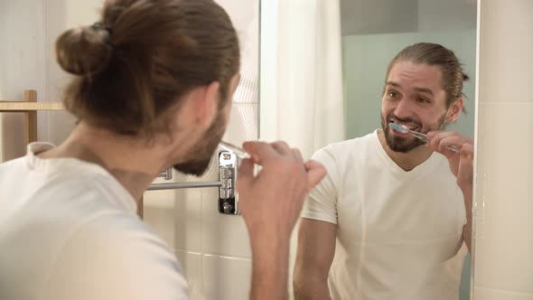 Man Brushing Teeth And Looking At Mirror In Bathroom