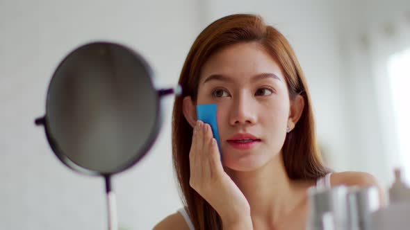 Asian young woman smile and looking in mirror doing skin care touch cheek using oil film