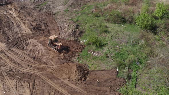 Aerial view of bulldozer flattening surface on further construction site