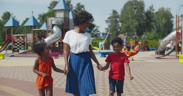 Afroamerican Mother and Two Children Walking at Kids Playground