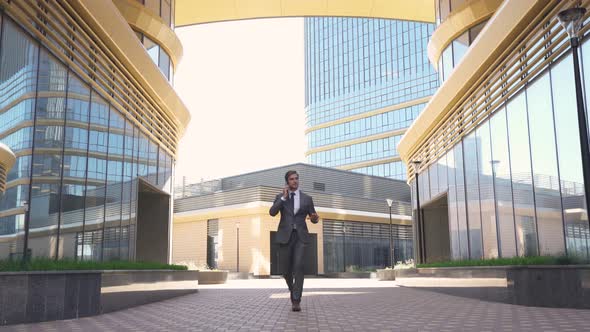 Young Businessman in a Suit Walking Next To the Glass Skyscraper and Talking on a Mobile Phone, Top