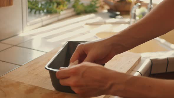 Chef greasing bread pan before he pours batter while baking in kitchen.