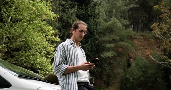 Young hipster man standing by his car using smartphone