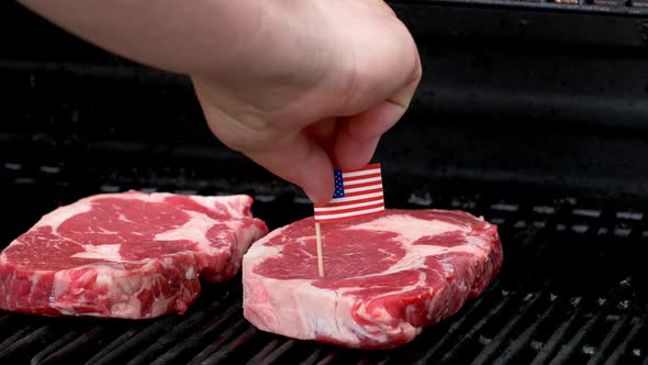 Two juicy rib-eye steaks sitting on the grill and cooking a hand comes in and sticks a tiny American