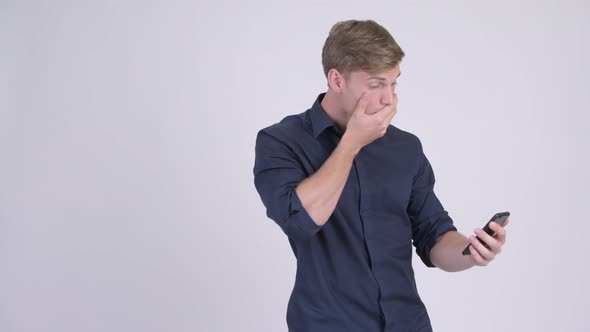 Young Handsome Blonde Businessman Using Phone and Looking Shocked