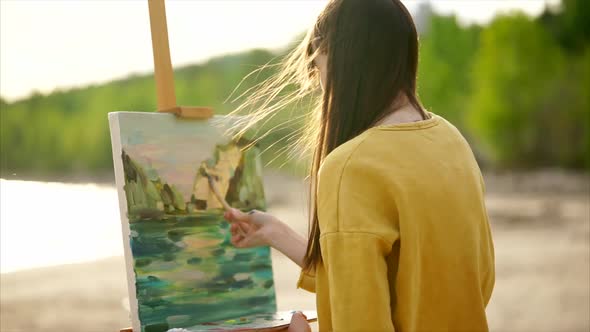 A Young Woman Paints a Painting on Canvas Which Stands on an Easel