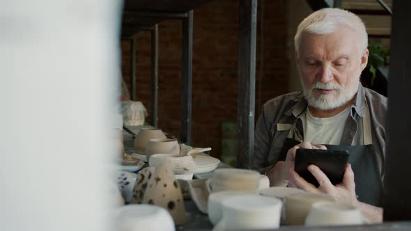 Portrait of Senior Craftsman Counting Hand-made Pots in Workshop and Using Tablet