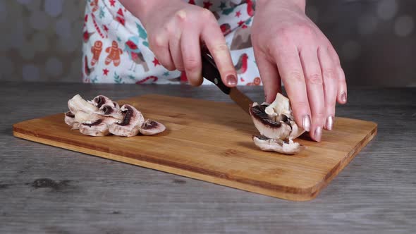 A woman in a kitchen cutting up a mushroom on a wooden chopping board