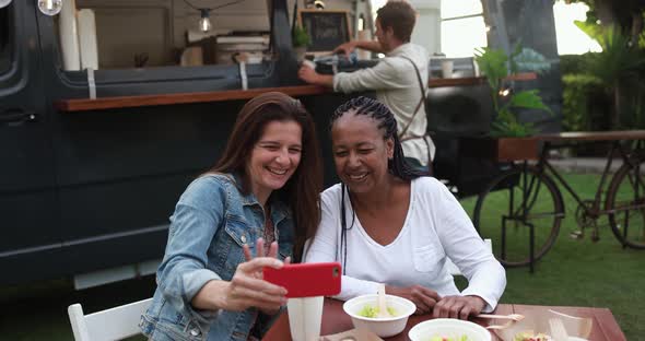 Multiracial women having fun taking photos with mobile phones at food truck restaurant outdoor