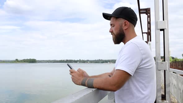 A young man stands on the bridge with a phone in his hands