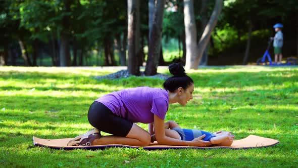 Mom massaging baby feet in green park in summer