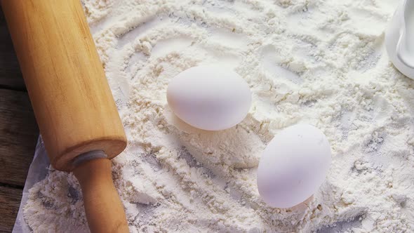 Flour, eggs and rolling pin placed over butter paper on a table