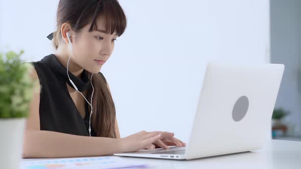 Young asian woman smiling sitting using laptop computer listening music with earphone.