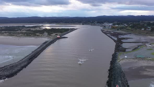 Two fishing boats leave port of Bandon, Oregon early morning. Panoramic aerial view of jetties, town