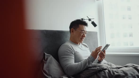 Smiling Asian man wearing eyeglasses typing by mobile