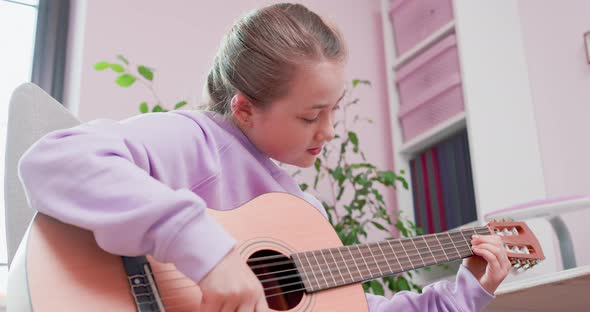 Teen Girl is Playing Guitar Sitting on the Floor in Front of the Tablet