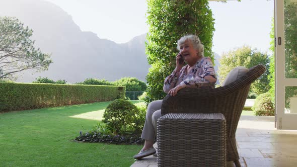 Caucasian senior woman smiling while talking on smartphone while sitting on the chair outdoors