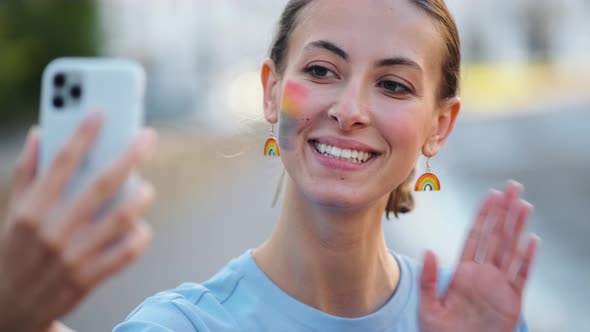 A lovely woman with rainbow make-up taking selfie photo using her phone during pride gay parade