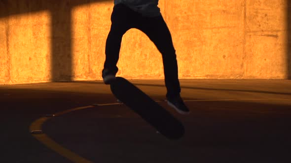 Silhouette of a young man skateboarding in a parking garage at sunset.