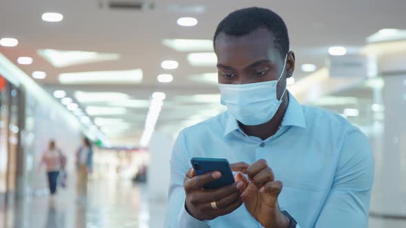 Man in a Protective Mask During an Epidemic Remains in Touch on the Internet on His Smartphone