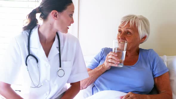 Female doctor serving a glass of water to senior woman in the bedroom