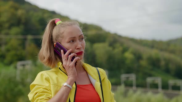 a Disgruntled Blonde in Red and Yellow Clothes is Talking on the Phone Against the Background of