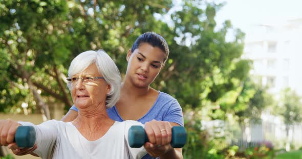 Female trainer assisting senior woman in exercising with dumbbells 4k