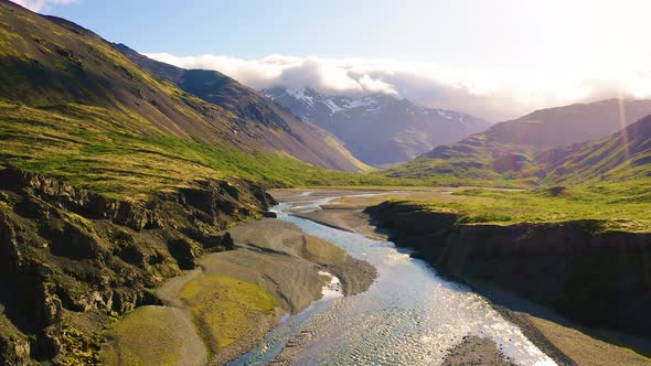 Flying Above a Glacial River in Iceland with Snowy Mountains in the Background