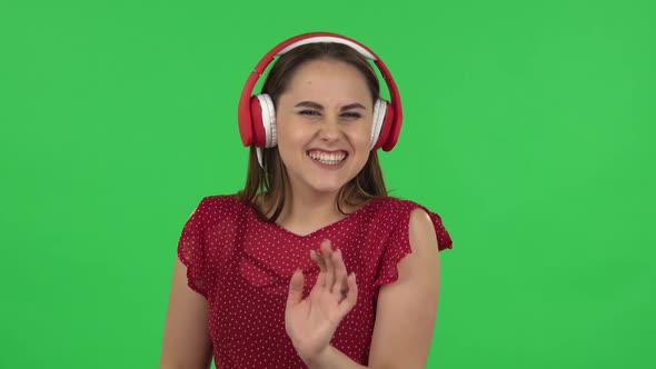 Portrait of Tender Girl in Red Dress Is Dancing and Enjoying Music in Big Red Headphones. Green