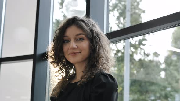 Curly Haired Woman Smiles and Poses for Camera By Window