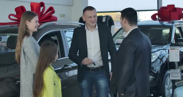 Positive Caucasian Dealer Giving Car Keys To Man, Shaking Clients' Hands. Cheerful Girl Showing