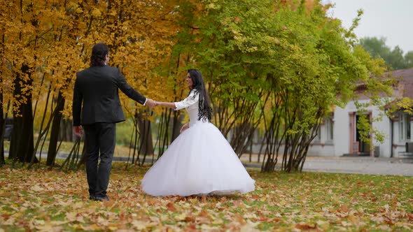 Bride and Groom are Dancing Outdoors in Autumn Day Wedding Suits in Park