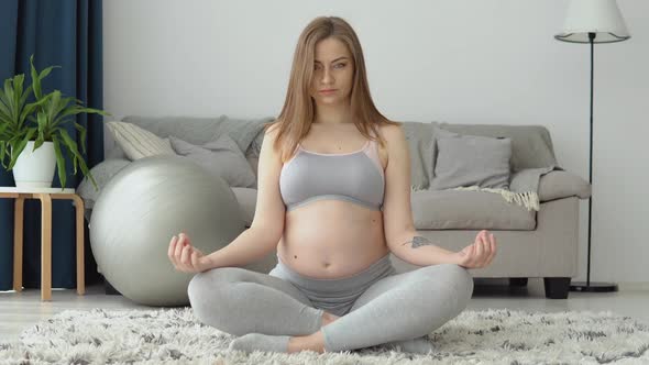 Pregnant Woman in Sportswear Sitting on the Carpet in the Lotus Position