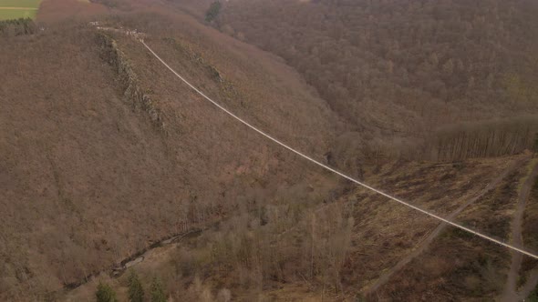Incredibly long suspension bridge hanging over a deep brown canyon during winter in Europe. Orbiting