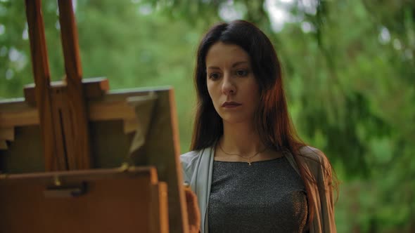 Portrait of Young Woman Painting a Landscape on Canvas at an Easel.