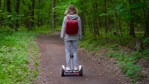 A Woman Rides Along a Forest Path on an Electric Gyrocopter. The Girl Has a Red Backpack and Light