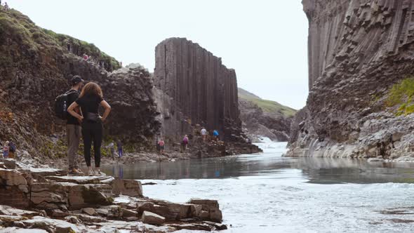 Basalt Columns in Background and Tourists Standing By Rocks Along the Riverside