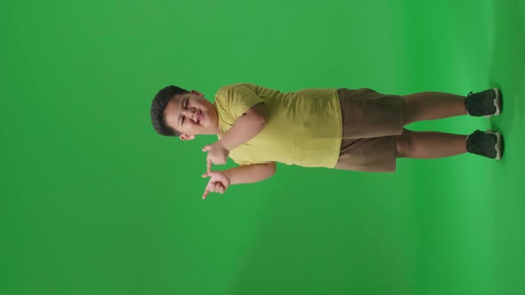 Asian Little Boy Smile And Pointing To The Side While Standing In The Green Screen Studio