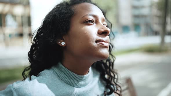 Handsome brunette African woman wearing blue sweater sitting on the bench