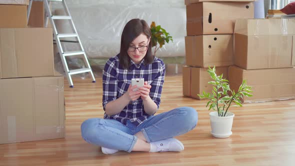 Young Woman Uses the Phone in the Background Boxes for Moving New Home