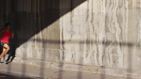 Fit african american man exercising in city, running under bridge