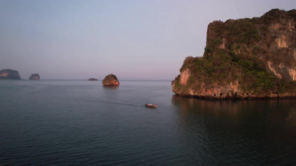 wide aerial shot of a single thai longtail boat motoring near large limestome mountains of Railay Be
